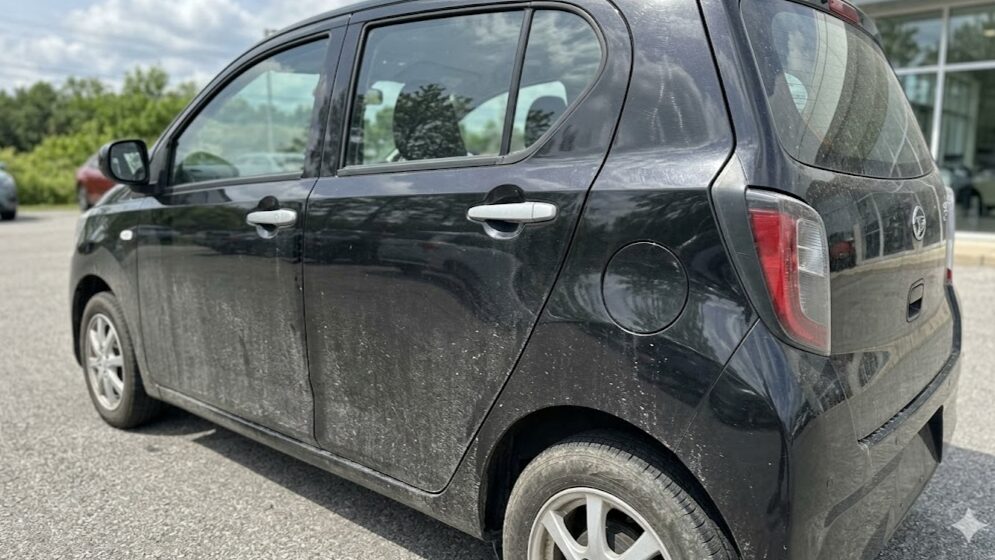 屋外駐車場で、砂ぼこりや水垢が目立つブラックマイカメタリックのミライース。黒色の維持の難しさを表現。